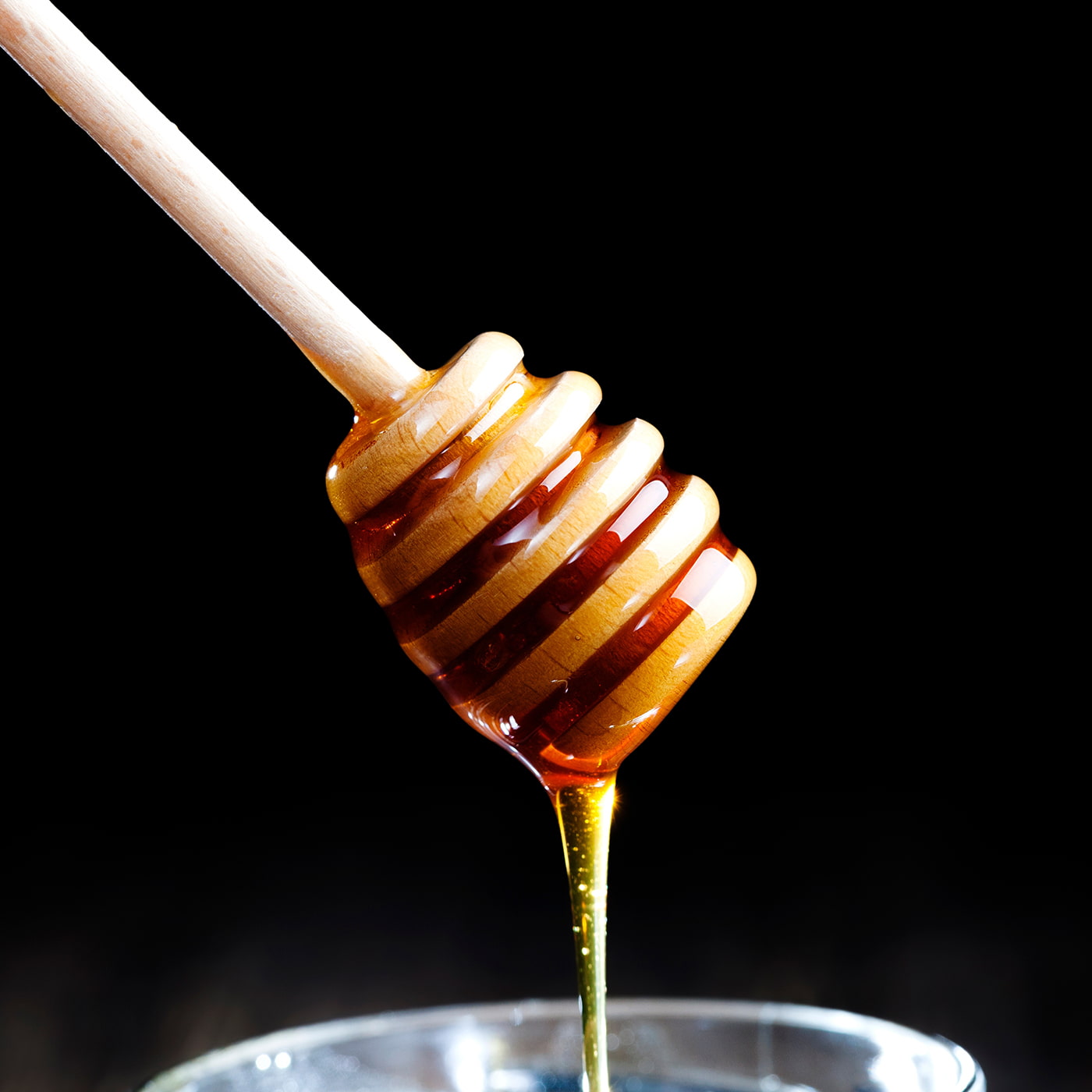 Pure Manuka honey dripping from a wooden honey dipper
